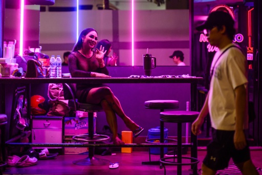 Emily (L), a sex worker, waves as she waits for clients in the back of a bar in Pattaya