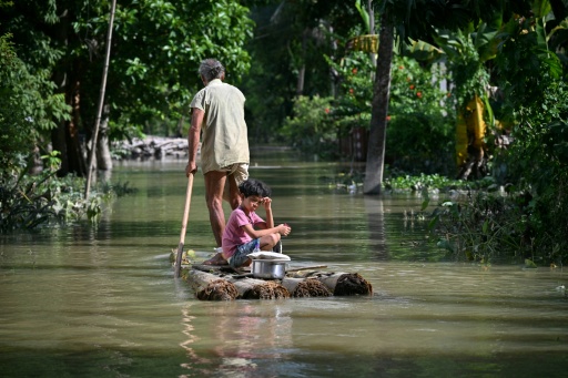 Un homme et une fillette  à bord d'un radeau de fortune,  sur une rivière en crure après des pluies de mousson torrentielles, dans un village du district de Sivasagar, dans l'Assam, en Inde,le 27 juillet 2026. — Biju BORO / AFP