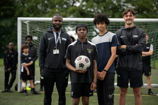 Matt Bishop (d) et Ezektel Agyemang (g), membres du programme "Football Beyond Borders", avec les élèves Fabian Myers (2e d) et Kaziah Cameron (2e g) après un match de foot au collège-lycée public Our Lady and St Chad Catholic Academy, à Wolverhampton, le 12 juin 2026 au Royaume-Uni