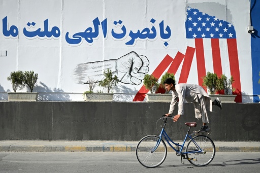 Un ciclista afgano realiza un truco mientras pasa frente a un mural en una pared que dice "Con ayuda divina, nuestra nación derrotó a Estados Unidos" en Kabul, el 15 de agosto de 2026, mientras el gobierno talibán celebra el quinto aniversario de su regreso al poder. — Wakil Kohsar / AFP