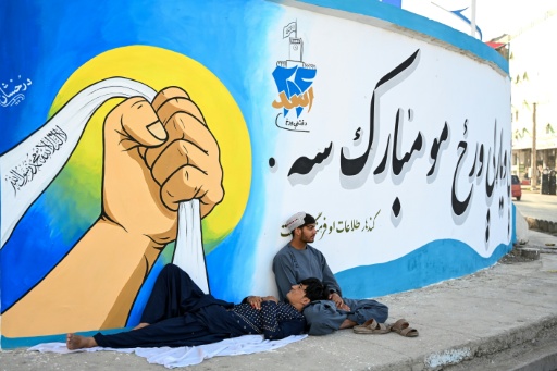 Hombres afganos se sientan junto a un mural que muestra consignas de la administración talibán en Kandahar el 12 de agosto de 2026, antes del quinto aniversario que marca su regreso al poder. — Sanaullah SEIAM / AFP