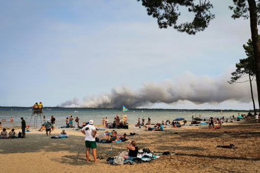 Des vacanciers sont assis sur la plage de Biscarrosse (sud-ouest), tandis qu'un épais nuage de fumée provoqué par un incendie s'élève dans le ciel, le 23 juillet 2026 — Maximilien LAMY / AFP
