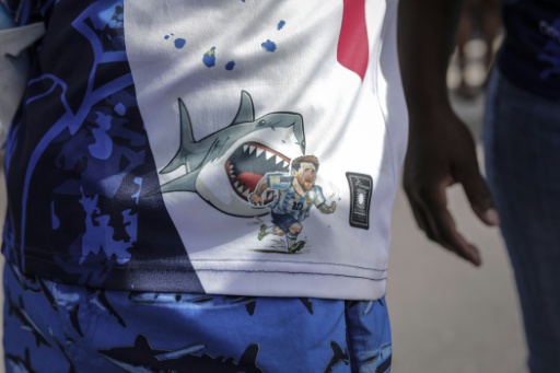 Un hincha de Cabo Verde con una camiseta en la que se ve a un tiburón, apodo de los jugadores de su selección, persiguiendo al argentino Lionel Messi. En Praia (Cabo Verde), el día del recibimiento al equipo tras caer en dieciseisavos de final del Mundial, el 5 de julio de 2026