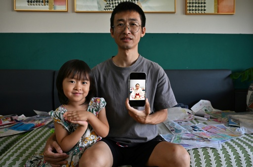 Ren Zhong shows a picture of his detained wife Wang Cong, a pastor at Zion Church, while sitting with his daughter at their house in Beihai, southern China's Guangxi province on July 29, 2026.
 Last October, Chinese authorities detained more than 20 of Zion's members, one of a series of similar clamp downs across the country recently. Zion Church is one of China's largest "underground" churches at which some Christians choose to worship instead of government-regulated ones. — - / AFP