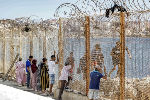 Des proches de migrants ayant traversé la frontière entre le Maroc et l'enclave espagnole de Ceuta voient passer des personnes refoulées derrière un grillage, dans la ville marocaine de Fnideq, le 2 août 2026 — Abdel Majid BZIOUAT / AFP