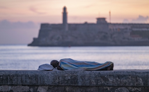 Una persona duerme envuelta en una sábana sobre el muro del Malecón al amanecer en La Habana, el 13 de agosto de 2026. Muchos cubanos pasan las noches de verano en espacios al aire libre en busca de alivio frente a las altas temperaturas y los frecuentes apagones. — YAMIL LAGE / AFP