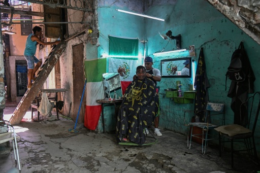 A barber cuts a customer's hair in his private business decorated with Mexican and Italian flags in the inner courtyard of a building in Havana on June 24, 2026