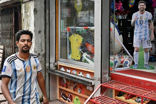 Torcedor de Bangladesh com a camisa da Argentina passa em frente a uma loja que exibe um pôster de Lionel Messi em Daca — MUNIR UZ ZAMAN / AFP
