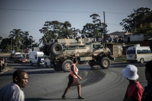 Des piétons passent devant un véhicule blindé de l'armée sud-africaine en patrouille dans une zone de Durban (Afrique du Sud) pillée lors d'émeutes antimigrants, le 1er juillet 2026 — MARCO LONGARI / AFP