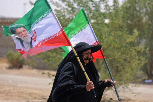 Une pèlerine iranienne brandit des drapeaux iraniens dont l'un comprend un portrait du guide suprême Ali Khamenei, tué dans un bombardement américain, le 29 juillet 2026 dans la ville-frontière de Zurbatiyah, en Irak — AHMAD AL-RUBAYE / AFP