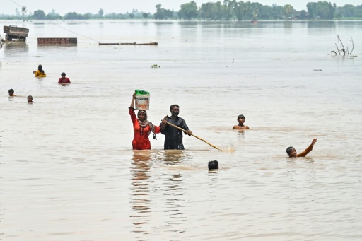 People wade through a flooded area after heavy monsoon rains induced a rise in the water level of the River Ravi in Pakistan's Muridke — Arif ALI / AFP