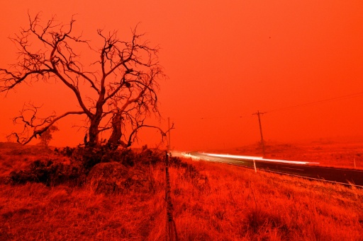 A long exposure picture shows a car commuting on a road as the sky turns red from smoke of the Snowy Valley bushfire on the outskirts of Cooma on January 4, 2020 — SAEED KHAN / AFP