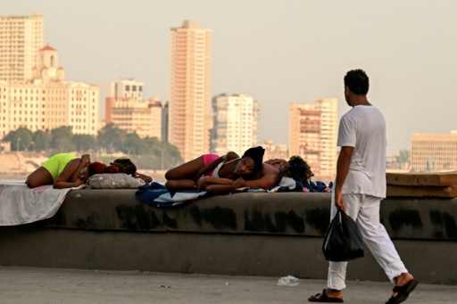 Un homme passe devant des femmes qui dorment sur le Malecon à La Havane lors d'une coupure de courant nationale, le 3 août 2026 — YAMIL LAGE / AFP