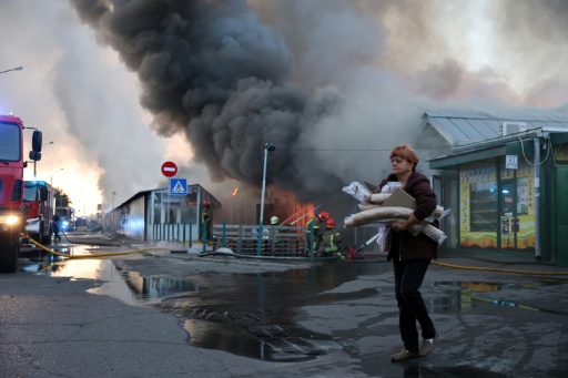 Une femme près d'un épais panache de fumée s'élevant depuis un marché aux livres après une attaque aérienne russe, le 16 août 2026 à Kiev — STRINGER / AFP
