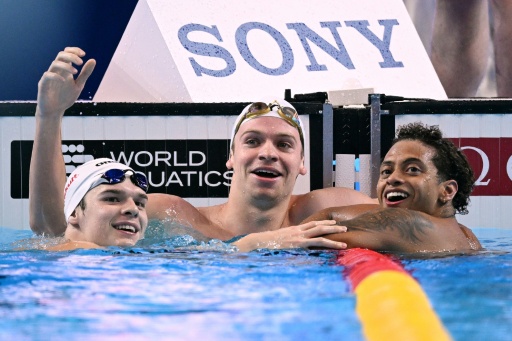 Léon Marchand (au centre) à côté de son ami et partenaire d'entraînement Hubert Kos (à gauche), et l'Américain  Shaine Casas après le 200 m 4 nages lors des championnats du monde de Singapour le 31 juillet 2025. — Oli SCARFF / AFP