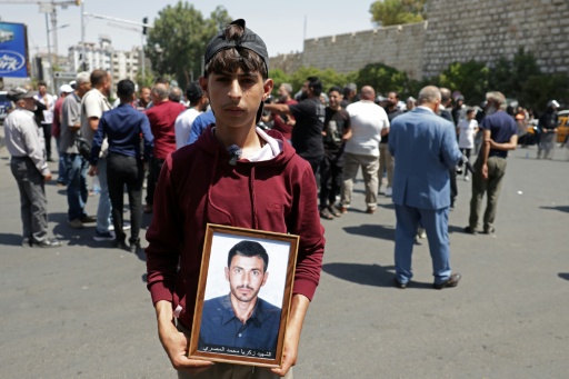 Un jeune Syrien porte la photo d'un proche, à proximité du tribunal de Damas où a été condamné à mort en son absence le président déchu Bachar al-Assad le 11 août 2026 — Bakr ALkasem / AFP