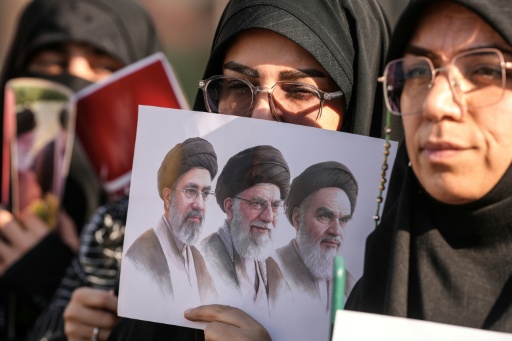 Des personnes en deuil tiennent une une photo du défunt fondateur de la République islamique, l'ayatollah Khomeini, du guide suprême défunt, l'ayatollah Khamenei, et de l'actuel guide suprême, Mojtaba Khamenei, lors du cortège funèbre de l'ayatollah Ali Khamenei à Nadjaf, le 8 juillet 2026 en Irak