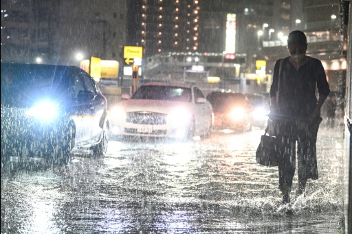 Des voitures dépassent un piéton sur une route inondée près de la station de métro de Chiba, dans la ville de Chiba à l'est de Tokyo, le 13 août 2026, alors que de fortes pluies s'abattaient sur la région — Philip FONG / AFP