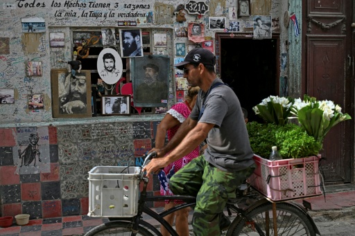 Una vendedora de flores pedalea junto a retratos del fallecido líder cubano Fidel Castro (1926-2016) y del revolucionario argentino Ernesto "Che" Guevara (1928-1967), colocados en la fachada de una vivienda en La Habana el 6 de agosto de 2026. El 13 de agosto se cumple el centenario del nacimiento de Castro, el dirigente que condujo la Revolución cubana durante casi medio siglo, mientras muchos de sus seguidores más fieles afrontan una de las peores crisis en décadas, marcada por apagones, escasez e inc