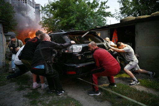 Varios hombres tratan de salvar un automóvil de un garaje en llamas en un edificio residencial alcanzado por un ataque ruso con misiles, el 6 de julio de 2026 en Kiev