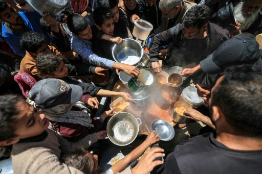 Displaced Palestinians receive food from a charity kitchen at a refugee camp in the central Gaza Strip in April 2026 — Eyad Baba / AFP