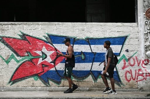 TDeux jeunes passent devant un mur arborant un drapeau cubain, le 14 juillet 2026 à La Havane, lors d'une panne d'électricité nationale à Cuba