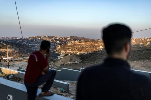 Des hommes palestiniens observent des soldats de l'armée israélienne depuis le toit d'une des maisons assiégées par des colons israéliens dans le village de Qusra, en Cisjordanie, le 18 août 2026 — ilia YEFIMOVICH / AFP
