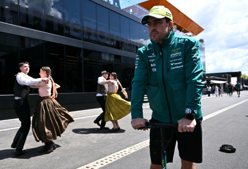 Fernando Alonso (derecha) pasa junto a bailarines con trajes típicos húngaros antes de la primera sesión de ensayos libres del Gran Premio de Hungría. En el circuito de Hungaroring en Mogyorod, cerca de Budapest, el 24 de julio de 2026 — Attila KISBENEDEK / AFP