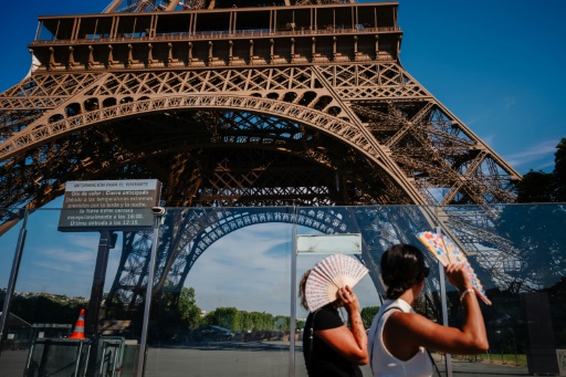 Des touristes se protègent du soleil avec des éventails en passant devant la tour Eiffel, fermée plus tôt en raison de la canicule, le 11 juillet 2026 à Paris — Dimitar DILKOFF / AFP