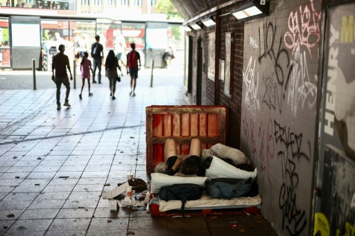 People walk past a man lying on a makeshift bed in a central London underpass — Henry NICHOLLS / AFP