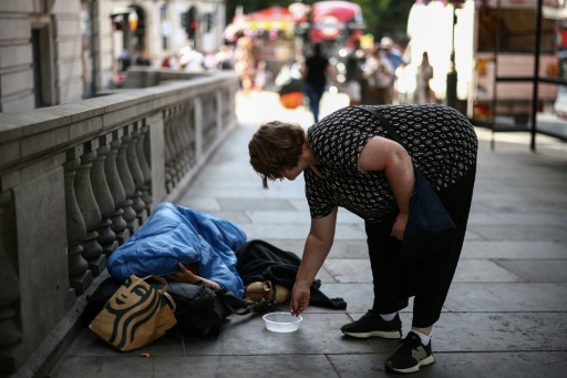 A woman puts some coins in a dish next to a man wrapped up with his dog on a London street — Henry NICHOLLS / AFP