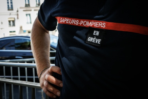 Un pompier avec "en grève" scratché sur la poitrine, devant  l'hôtel de Beauvau, à Paris, le 13 août 2026 — SIMON WOHLFAHRT / AFP