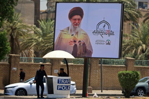 Agentes de tránsito montan guardia bajo una valla publicitaria gigante con una imagen del difunto líder supremo de Irán, el ayatolá Ali Jamenei, junto a un cruce de carreteras en Bagdad el 2 de julio de 2026, antes de su funeral en Teherán