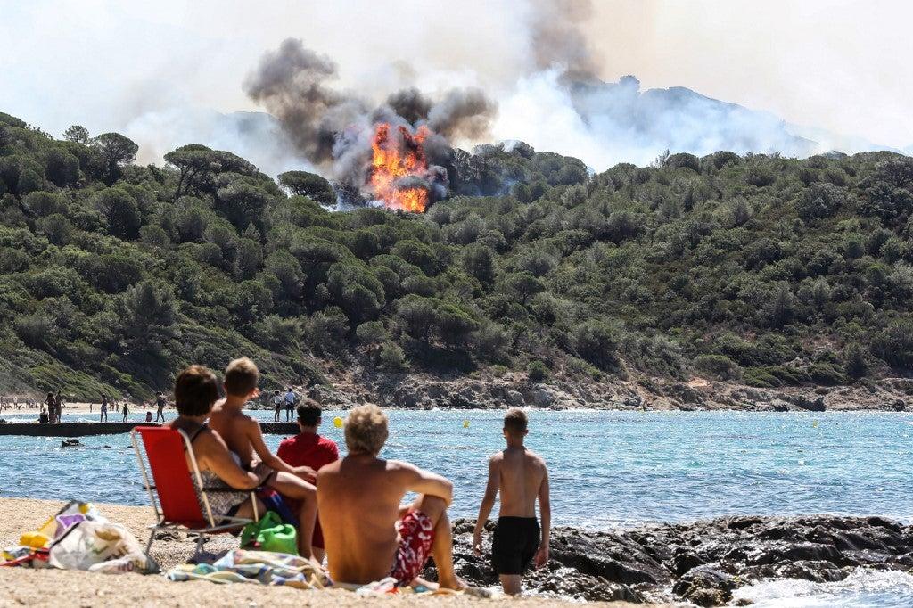 Pessoas aproveitam da praia enquanto olham para um incêndio florestal em La Croix-Valmer, perto de Saint-Tropez, em 25 de julho de 2017. Valery HACHE / AFP