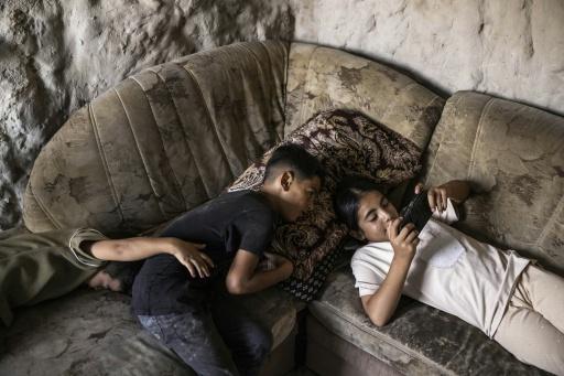 الطفل الفلسطيني وحيد (وسط) مع شقيقته التي تلهو بألعاب الفيديو داخل كهف حولته أسرته إلى منزل في قرية التواني في الضفة الغربية المحتلة في 11 أيلول/سبتمبر 2026 — جون ويسلز