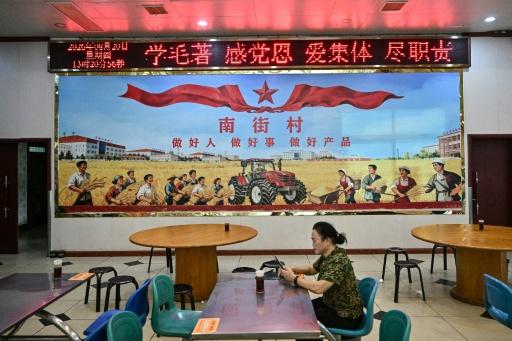 A woman checking her phone in front of a socialist inspired mural at a restaurant in Nanjie Commune, in central China's Henan province — Pedro PARDO / AFP