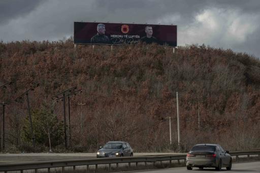 A giant banner depicting former Kosovan president Hashim Thaci (L) and former parliament speaker Kadri Veseli and reading "Heroes of War and Peace" is seen near the village of Komoran on February 5, 2026. — Armend NIMANI / AFP