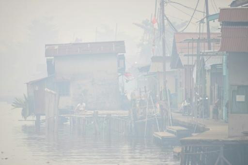 A man sits by the Kapuas river as thick smoke and haze shrouds the city of Pontianak in West Kalimantan — BAY ISMOYO / AFP